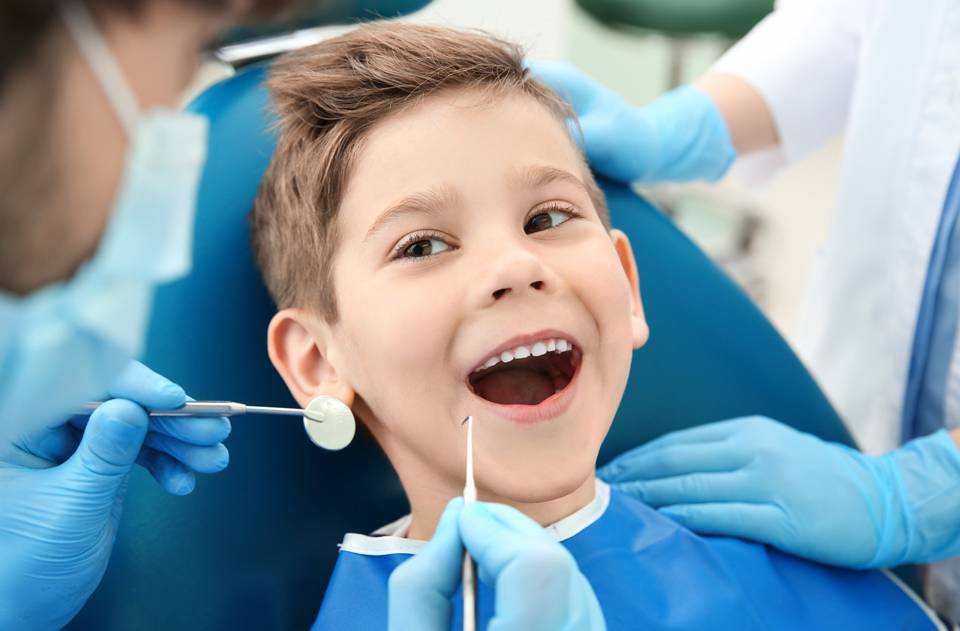 child smiling in a dentist chair while the dentist prepares to perform a cleaning